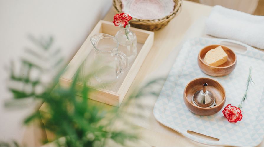A practical life tray with a small glass jug, wooden bowls and a flower